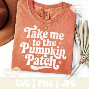 Pode incluir: Camiseta laranja Comfort Colors com o texto branco "Take me to the Pumpkin Patch". A camisa tem gola redonda e mangas curtas. Um colar de ouro com um pingente está sobre a camisa. Um chapéu marrom é visível no canto superior esquerdo.