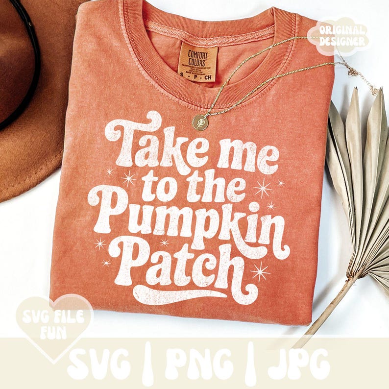 May include: Orange Comfort Colors t-shirt with the text "Take me to the Pumpkin Patch" in white. The shirt has a crew neck and short sleeves. A gold necklace with a pendant is draped on the shirt. A brown hat is visible in the upper left corner.
