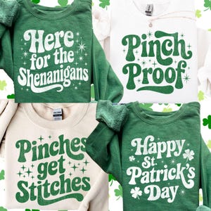 Op de afbeelding: Vier sweatshirts met ontwerpen met het thema St. Patrick's Day. Een groene sweatshirt zegt "Here for the Shenanigans", een witte sweatshirt zegt "Pinch Proof", een tan sweatshirt zegt "Pinches get Stitches" en een groene sweatshirt zegt "Happy St. Patrick's Day".