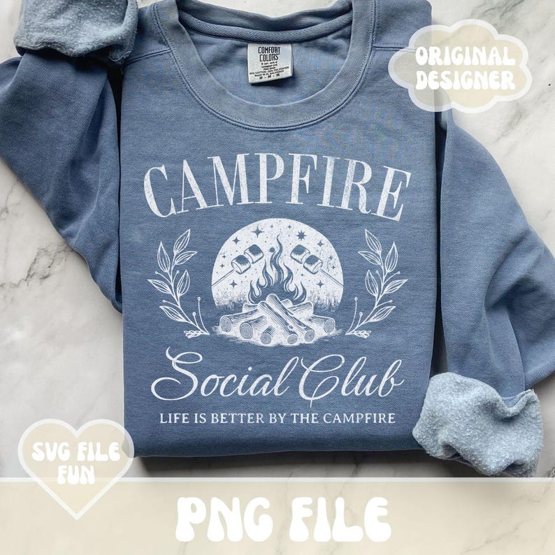 Może przedstawiać: Niebieska bluza z białym nadrukiem przedstawiającym ognisko z piankami, gwiazdami i tekstem "Campfire Social Club" oraz "Life is better by the campfire".
