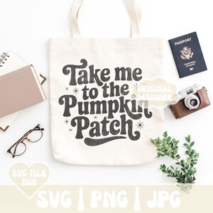 May include: Cream-colored tote bag with the text "Take me to the Pumpkin Patch" in a retro font. The image includes a passport, camera, glasses, and other accessories, suggesting a fall theme.