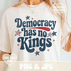 Könnte beinhalten: Cremefarbenes T-Shirt mit dem Text "Democracy has no Kings" in Marineblau, Rot und Weiß. Das Design beinhaltet Sterne und einen roten Streifen, die ein patriotisches Thema hervorrufen. Das Shirt hat einen Vintage-Look.