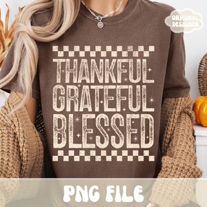 Może przedstawiać: Brązowa koszulka z napisami "THANKFUL, GRATEFUL, BLESSED" w postarzanym, złamanym białym kroju pisma. Tekst jest obramowany wzorem w szachownicę. Koszulka ma r&oacute;wnież napis "PNG FILE" na dole i "ORIGINAL DESIGNER" w prawym g&oacute;rnym rogu.