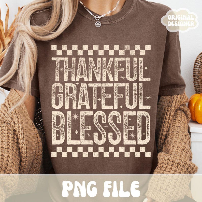Może przedstawiać: Brązowa koszulka z napisami "THANKFUL, GRATEFUL, BLESSED" w postarzanym, złamanym białym kroju pisma. Tekst jest obramowany wzorem w szachownicę. Koszulka ma r&oacute;wnież napis "PNG FILE" na dole i "ORIGINAL DESIGNER" w prawym g&oacute;rnym rogu.