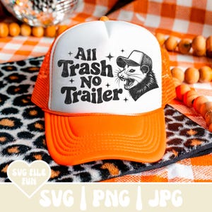May include: A trucker hat with a white front panel and an orange brim and mesh back. The hat features the text "All Trash No Trailer" and a graphic of a possum wearing a hat. The hat is on a leopard print surface.