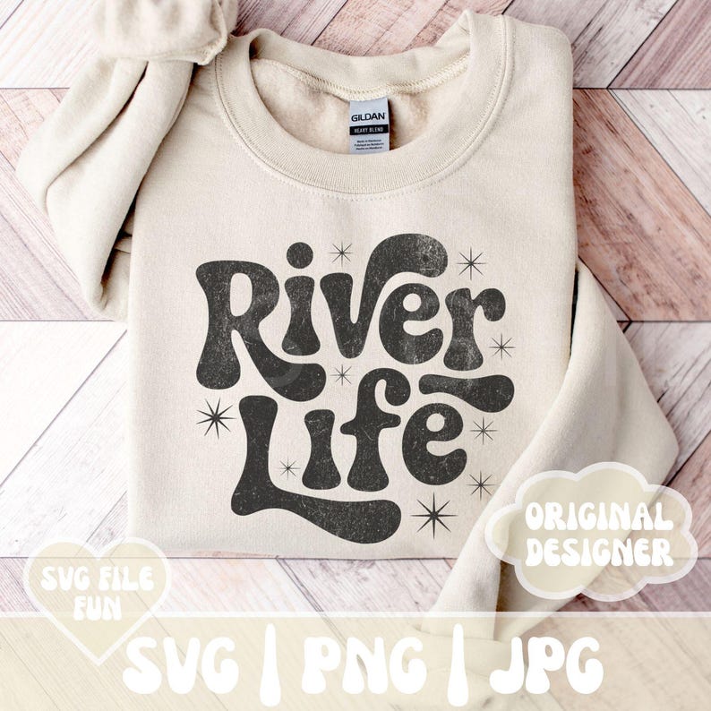 May include: A beige sweatshirt with the words "River Life" in a retro font. The text is black with a distressed texture and surrounded by starburst graphics. The sweatshirt also has the text "SVG FILE FUN" and "ORIGINAL DESIGNER".