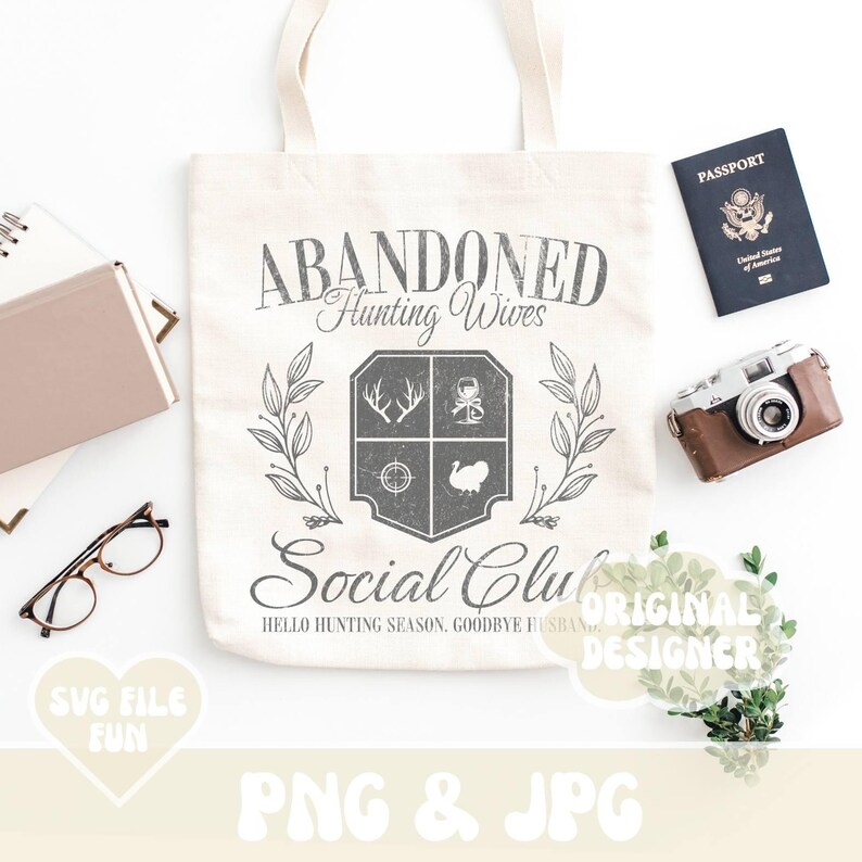 Może przedstawiać: Biała torba typu tote z szarym wzorem, na kt&oacute;rym widnieje napis "Abandoned Hunting Wives Social Club" oraz herb z motywami związanymi z polowaniem. Tekst pod herbem brzmi "Hello Hunting Season, Goodbye Husbands".