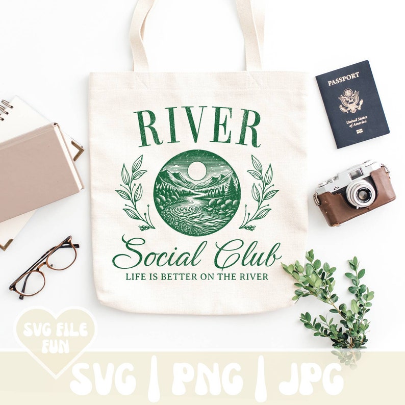 May include: Cream-colored tote bag with a green graphic that reads "RIVER Social Club" and "Life is better on the river." The design features a river scene. A passport, camera, and greenery are also present.