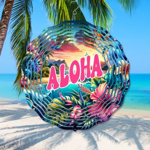 Peut inclure: Un mobile à vent en métal coloré avec une scène tropicale et le mot "ALOHA" en lettres roses. Le mobile a un design en couches avec un fond bleu et des feuilles vertes.