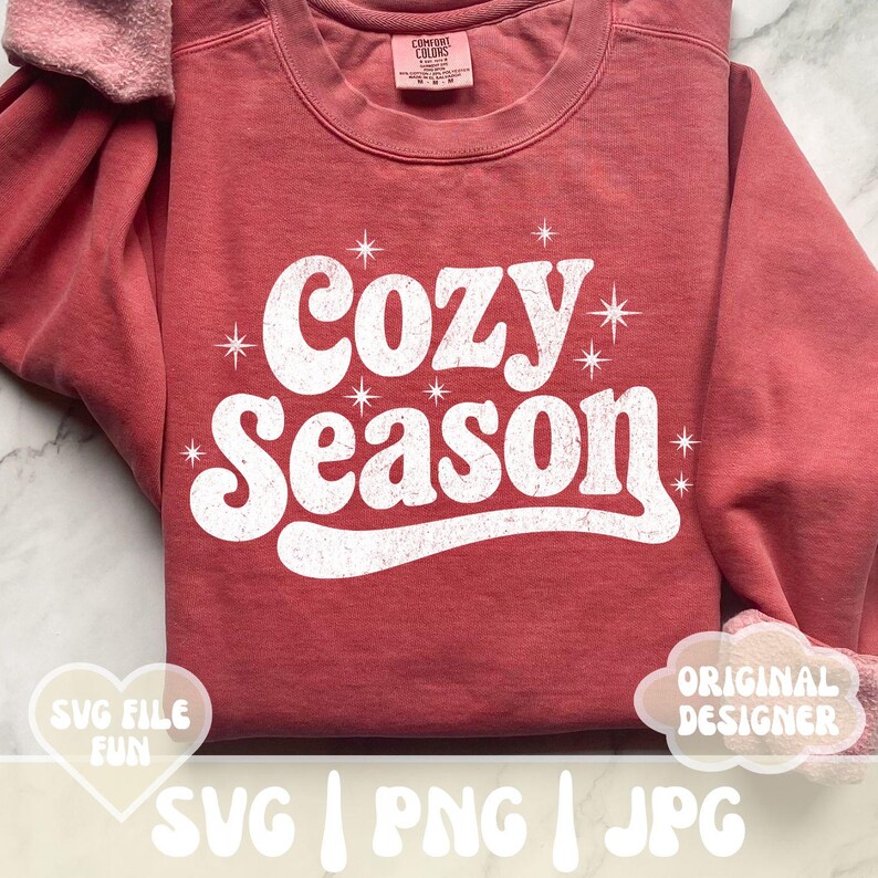 Puede incluir: Una sudadera de color rojo anaranjado con la frase "Cozy Season" en blanco, con letras de estilo retro. El dise&ntilde;o incluye detalles de estrellas. La sudadera tiene cuello redondo y mangas largas. La imagen tambi&eacute;n incluye el texto "SVG FILE FUN" y "ORIGINAL DESIGNER".