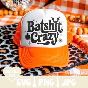 May include: Orange and white trucker hat with the phrase "Batshit Crazy" in black, featuring bat and star graphics. The hat has a mesh back and a curved brim. A fun accessory for Halloween or a casual look.
