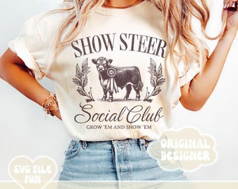May include: A white t-shirt with a black and white illustration of a steer with the text "Show Steer Social Club Grow 'Em and Show 'Em" printed on the front. The text "Original Designer" is in a speech bubble in the bottom right corner.