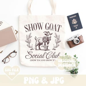 May include: A white tote bag with a brown goat illustration and the text "Show Goat Social Club Grow 'em and Show 'em". The bag is on a white surface with a passport, camera, and greenery.