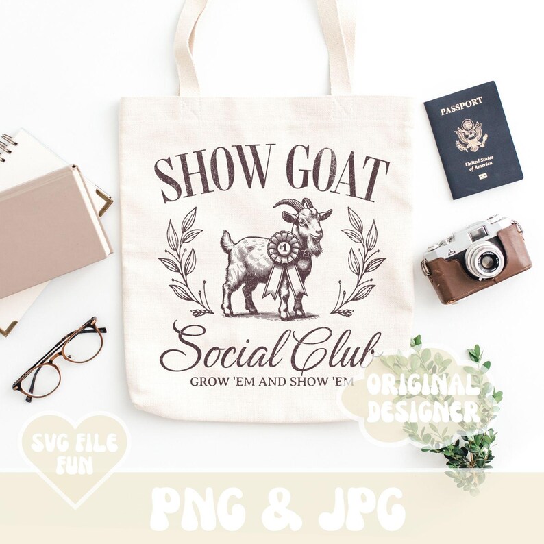 May include: A white tote bag with a brown goat illustration and the text "Show Goat Social Club Grow 'em and Show 'em". The bag is on a white surface with a passport, camera, and greenery.