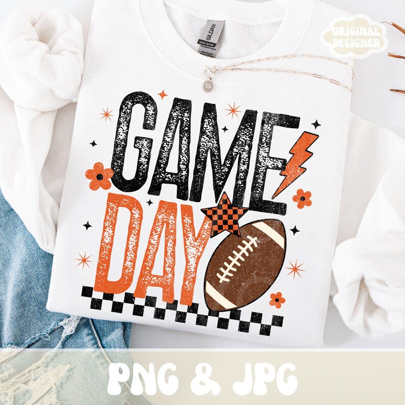 May include: White sweatshirt with the words "GAME DAY" in black and orange, along with a football graphic. The design includes a checkered star, lightning bolt, and floral accents. The phrase "PNG & JPG" is at the bottom.