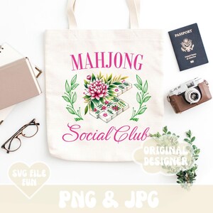 Puede incluir: Una bolsa de tela blanca con el texto "Mahjong Social Club" en letras rosas. Un dise&ntilde;o floral con flores rosas y hojas verdes rodea un juego de fichas de mahjong.