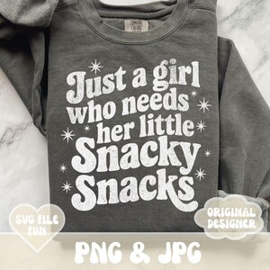 May include: A charcoal gray sweatshirt with the text "Just a girl who needs her little Snacky Snacks" in white, with star accents. The sweatshirt also has the text "SVG FILE FUN" and "ORIGINAL DESIGNER".