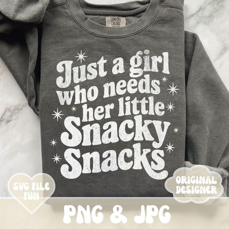 May include: A charcoal gray sweatshirt with the text "Just a girl who needs her little Snacky Snacks" in white, with star accents. The sweatshirt also has the text "SVG FILE FUN" and "ORIGINAL DESIGNER".