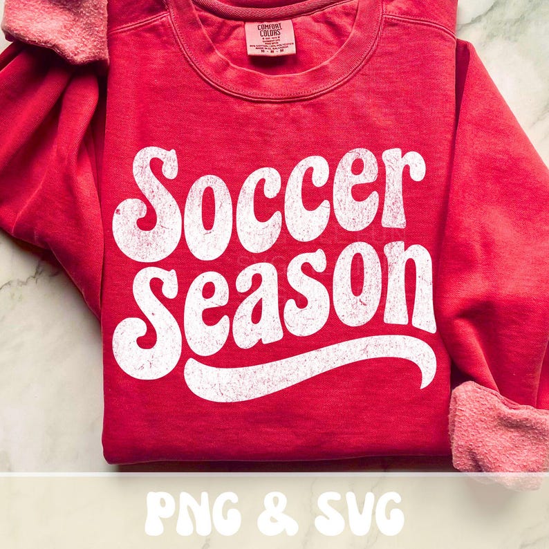 Op de afbeelding: Een rode sweatshirt met de tekst "Soccer Season" in grote, witte letters in retrostijl. De sweatshirt heeft een ronde hals en lange mouwen met geribde manchetten. De afbeelding bevat ook de tekst "PNG & SVG".