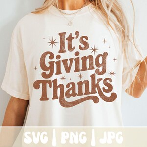 May include: Cream-colored t-shirt with the phrase "It's Giving Thanks" in brown, retro-style lettering. The design includes starburst and cross accents. The bottom of the shirt displays "SVG | PNG | JPG".
