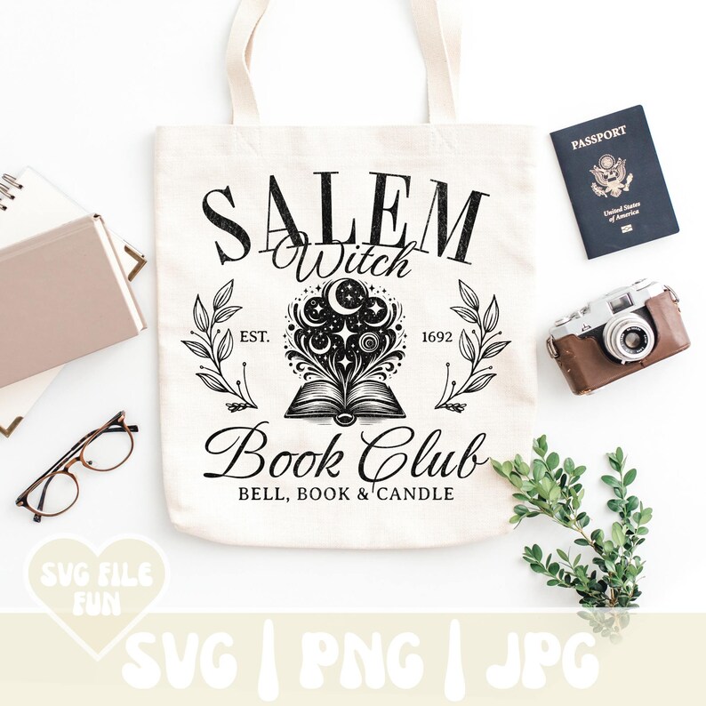 K&ouml;nnte beinhalten: Eine wei&szlig;e Einkaufstasche mit einem schwarzen Design, auf dem "Salem Witch Book Club Est. 1692 Bell, Book & Candle" steht. Das Design zeigt ein Buch, aus dem ein Mond und Sterne herauskommen.