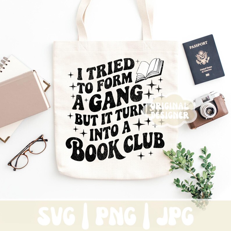 May include: Cream-colored tote bag with the text "I tried to form a gang but it turned into a book club" in black. The bag is surrounded by a passport, a camera, glasses, and a notebook.