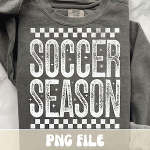 K&ouml;nnte beinhalten: Dunkelgraues Sweatshirt mit dem Text "SOCCER SEASON" in abgenutzten wei&szlig;en Buchstaben. Der Text wird von einem Schachbrettmuster umrahmt. Das Sweatshirt hat einen Rundhalsausschnitt und lange &Auml;rmel. Unten steht "PNG FILE".