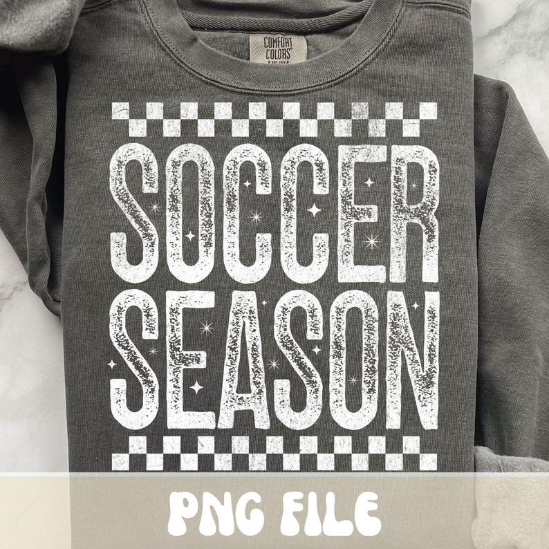 K&ouml;nnte beinhalten: Dunkelgraues Sweatshirt mit dem Text "SOCCER SEASON" in abgenutzten wei&szlig;en Buchstaben. Der Text wird von einem Schachbrettmuster umrahmt. Das Sweatshirt hat einen Rundhalsausschnitt und lange &Auml;rmel. Unten steht "PNG FILE".