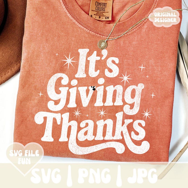 May include: A coral-colored t-shirt with the phrase "It's Giving Thanks" in white, retro-style lettering. The shirt features starburst accents and the text "SVG FILE FUN" and "SVG | PNG | JPG". A gold necklace is draped on the shirt.