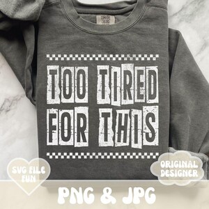 以下が含まれることがあります： グレーのトレーナーに、白いブロック体で「Too Tired For This」という文字が書かれています。文字は、白黒の市松模様の枠で囲まれています。