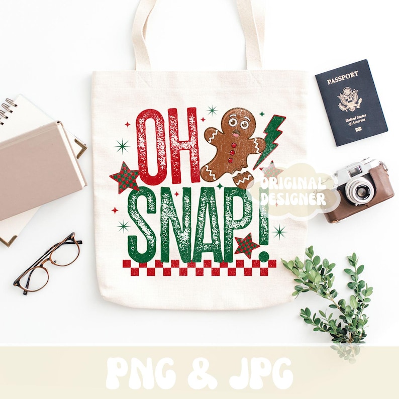 May include: A white tote bag with the text "OH SNAP!" in red and green, featuring a gingerbread man and a lightning bolt. The bag is surrounded by a passport, camera, and greenery.