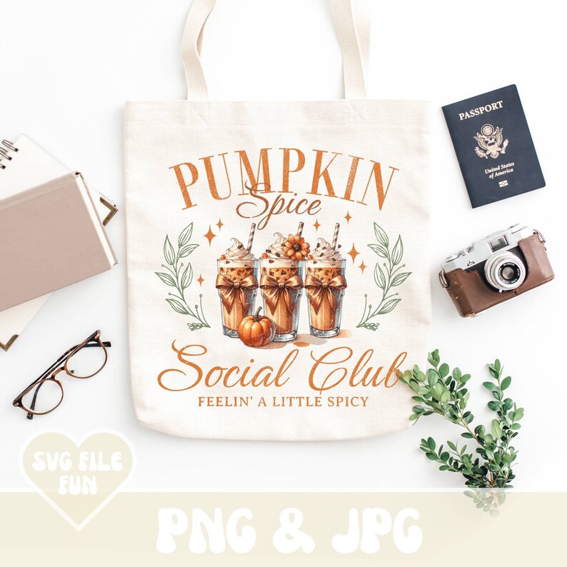 May include: Cream-colored tote bag with the text "PUMPKIN SPICE Social Club" and a graphic of three pumpkin spice lattes. The bag also has the text "FEELIN' A LITTLE SPICY". A passport, camera, and glasses are next to the bag.