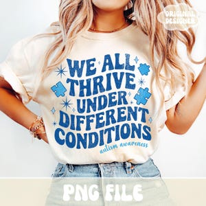 May include: Cream-colored t-shirt with the text "WE ALL THRIVE UNDER DIFFERENT CONDITIONS" in blue, along with puzzle pieces and starburst graphics. The phrase "autism awareness" is printed below the main text. The shirt has rolled-up sleeves.