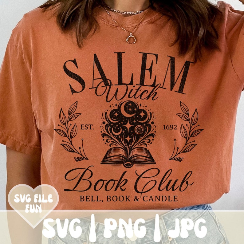K&ouml;nnte beinhalten: Ein rostfarbenes T-Shirt mit einem schwarzen Grafikdesign, auf dem "Salem Witch Book Club" mit einem Buch, Sternen und Monden steht. Der Text lautet au&szlig;erdem "Est. 1692" und "Bell, Book & Candle".