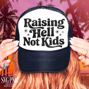 May include: Black and white trucker hat with the text "Raising Hell Not Kids" in a bold, retro font. The hat has a white front panel and a black mesh back. The design includes star accents.