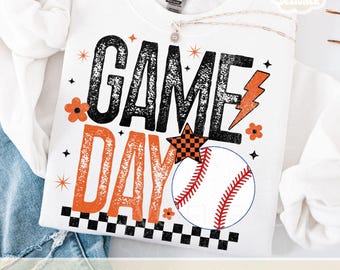 May include: White sweatshirt with the words "GAME DAY" in black and orange, a baseball graphic, and decorative stars and flowers. The design includes a lightning bolt and a checkered star. The words "PNG & JPG" are at the bottom.