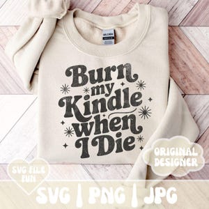 May include: A cream-colored sweatshirt with the text "Burn my Kindle when I Die" in a retro font. The design includes starburst and star accents. The sweatshirt also has the text "SVG FILE FUN" and "ORIGINAL DESIGNER".