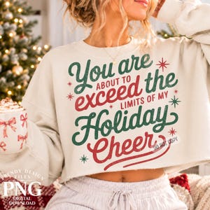 May include: A cream-colored cropped sweatshirt featuring the text "You are ABOUT TO exceed the LIMITS OF MY Holiday Cheer" in dark green and red lettering, accented with small red and green star-shaped symbols throughout the design.