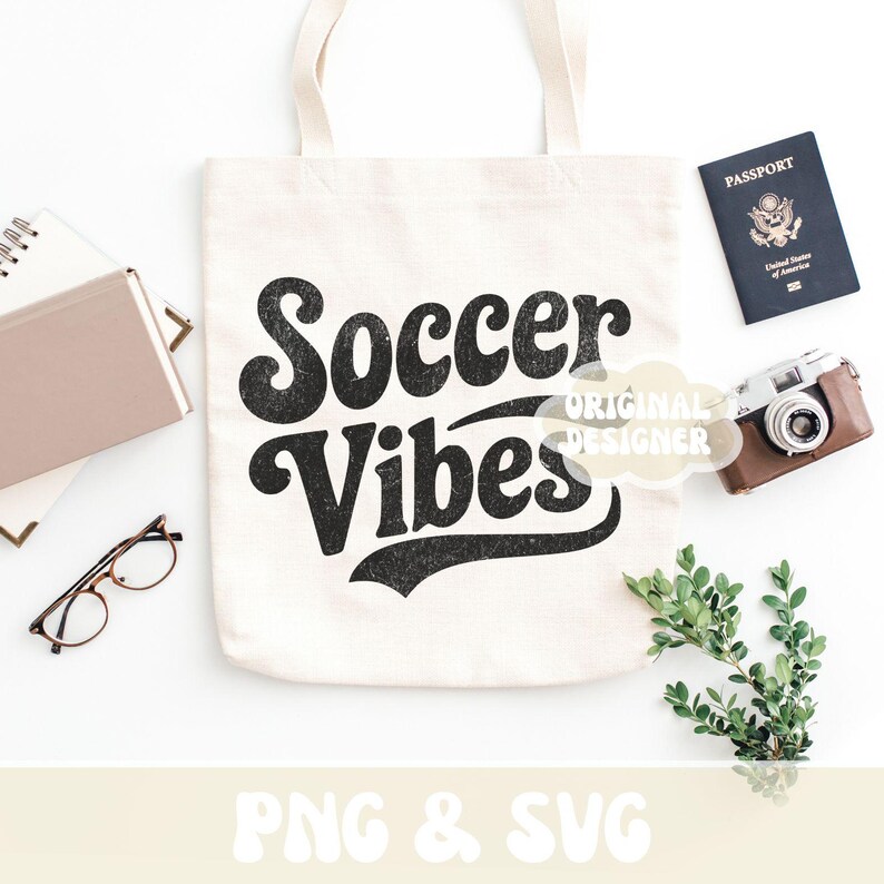 Op de afbeelding: Een cr&egrave;mekleurige draagtas met de woorden "Soccer Vibes" in een zwarte retro-lettertype. Een paspoort, camera, bril, notitieboek en groen omringen de tas. De woorden "Original Designer" zijn ook zichtbaar.