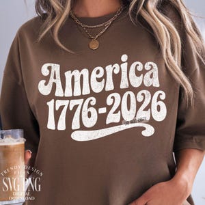 May include: A brown sweatshirt with the text "America 1776-2026" in a distressed white font. The sweatshirt also has the text "Do Not Copy" in a smaller font. The design is a vintage style.