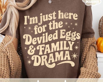 May include: A brown t-shirt with the text "I'm just here for the Deviled Eggs & FAMILY DRAMA" in a retro font. The shirt also has the words "SVG | PNG | JPG" at the bottom and "ORIGINAL DESIGNER" in the upper right corner.