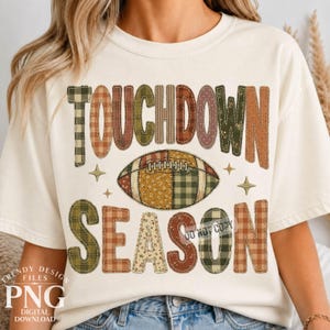 May include: A cream-colored short-sleeve t-shirt featuring the text TOUCHDOWN SEASON in a patchwork style with various patterns including plaid, floral, and solid earth tones. A central football graphic matches the patchwork design.
