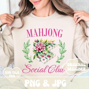 Puede incluir: Una sudadera beige con el texto "Mahjong Social Club" en letras rosas. El dise&ntilde;o presenta un arreglo floral con una flor rosa y hojas verdes, y un juego de fichas de mahjong. El texto "PNG & JPG" tambi&eacute;n est&aacute; incluido en letras rosas.