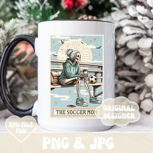 May include: White ceramic mug with a black handle. The mug features a colorful illustration of a skeleton wearing a blue shirt and sitting on a bench with a soccer ball. The text "The Soccer Mom" is printed on the mug.