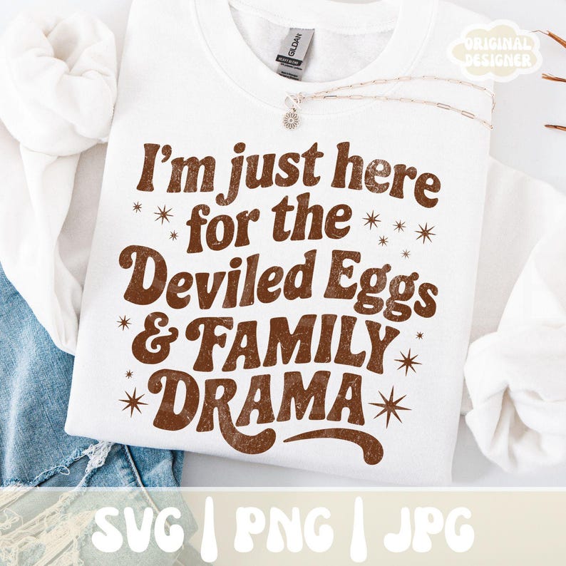 Puede incluir: Sudadera blanca con el texto "I'm just here for the Deviled Eggs & FAMILY DRAMA" en letras marrones. El dise&ntilde;o incluye acentos de estrellas. La sudadera es de la marca Gildan.