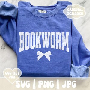May include: A blue sweatshirt with the text "BOOKWORM" in white with a white bow underneath. The sweatshirt has a white tag that says "COMFORT COLORS" on it. The text "SVG | PNG | JPG" is at the bottom of the image.