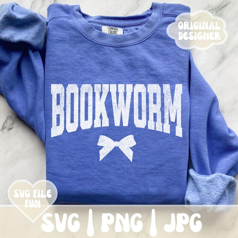 May include: A blue sweatshirt with the text "BOOKWORM" in white with a white bow underneath. The sweatshirt has a white tag that says "COMFORT COLORS" on it. The text "SVG | PNG | JPG" is at the bottom of the image.