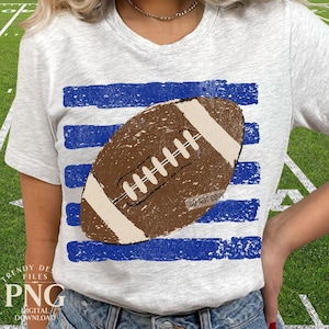 K&ouml;nnte beinhalten: Ein hellgrau meliertes Kurzarm-T-Shirt mit einem Grafikdruck eines braunen American Footballs, der &uuml;ber horizontalen, abgenutzten blauen Streifen zentriert ist. Das Football-Design enth&auml;lt wei&szlig;e Schn&uuml;rsenkel und wei&szlig;e Endstreifen mit einem kleinen DO NOT COPY Wasserzeichen.