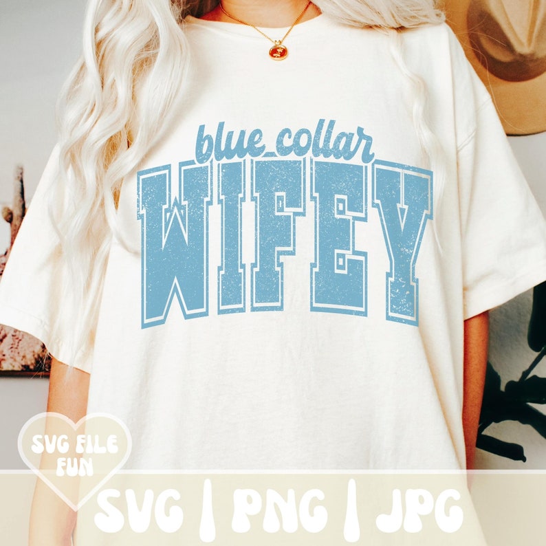 Op de afbeelding: Een off-white t-shirt met de tekst blue collar WIFEY in een verweerd lichtblauw collegiaal lettertype. De afbeelding is gecentreerd op de borst. Een hartvormige afbeelding in de hoek bevat de tekst SVG FILE FUN SVG PNG JPG.
