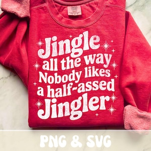 May include: Red sweatshirt with white text that reads "Jingle all the way Nobody likes a half-assed Jingler." The text is surrounded by starburst graphics. The sleeves are cuffed. The shirt is made of a soft material.